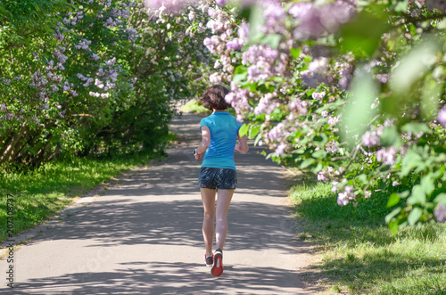 Woman runner jogging in spring park with lilac blossom, morning run outdoors, fitness and running healthy lifestyle concept 