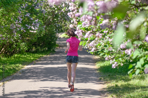 Woman runner jogging in spring park with lilac blossom, morning run outdoors, fitness and running healthy lifestyle concept 