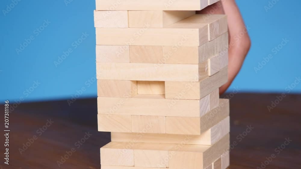 hands of Young man plays jenga on blue background, close-up. A man builds a tower of blocks while playing jenga hands of Young man plays jenga on blue background, close-up. A man builds a tower of blocks while playing jenga