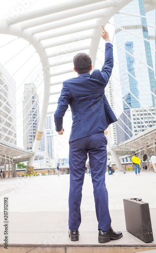 Businessman raising his fist  in the air, with office building background - business success, achievement, and win concepts