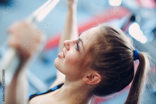Young woman exercising pulling down lateral pull-down weights exercising machine. Fitness in gym.