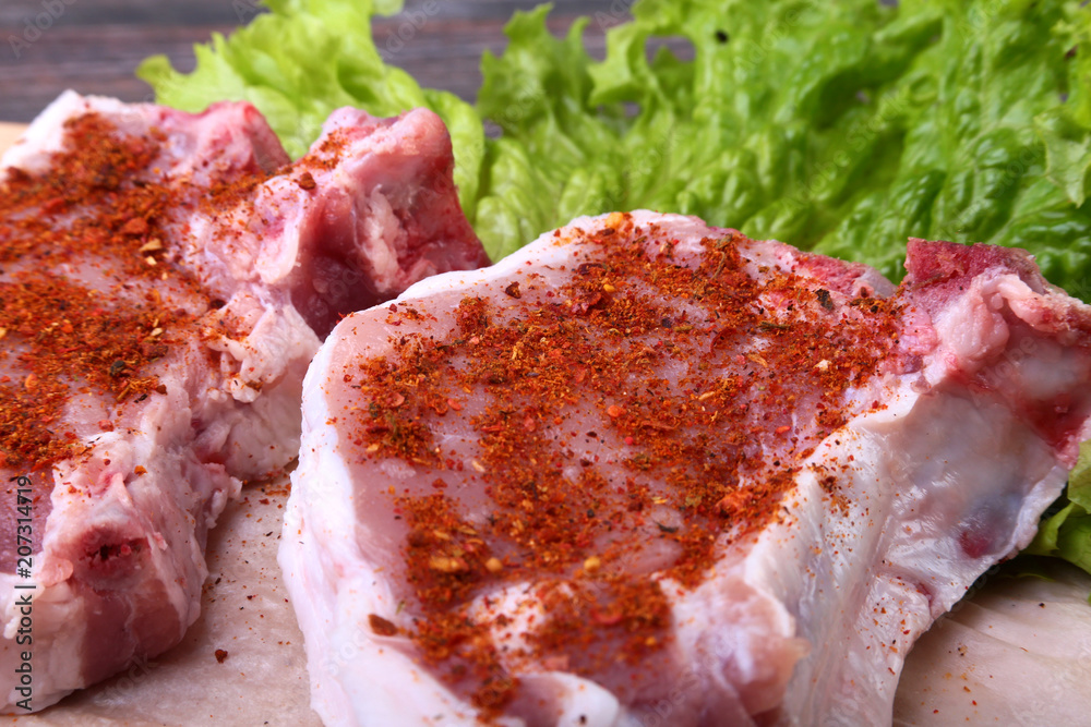 Raw pork steak with spices Leaves lettuce on wooden cutting board. Ready for cooking.