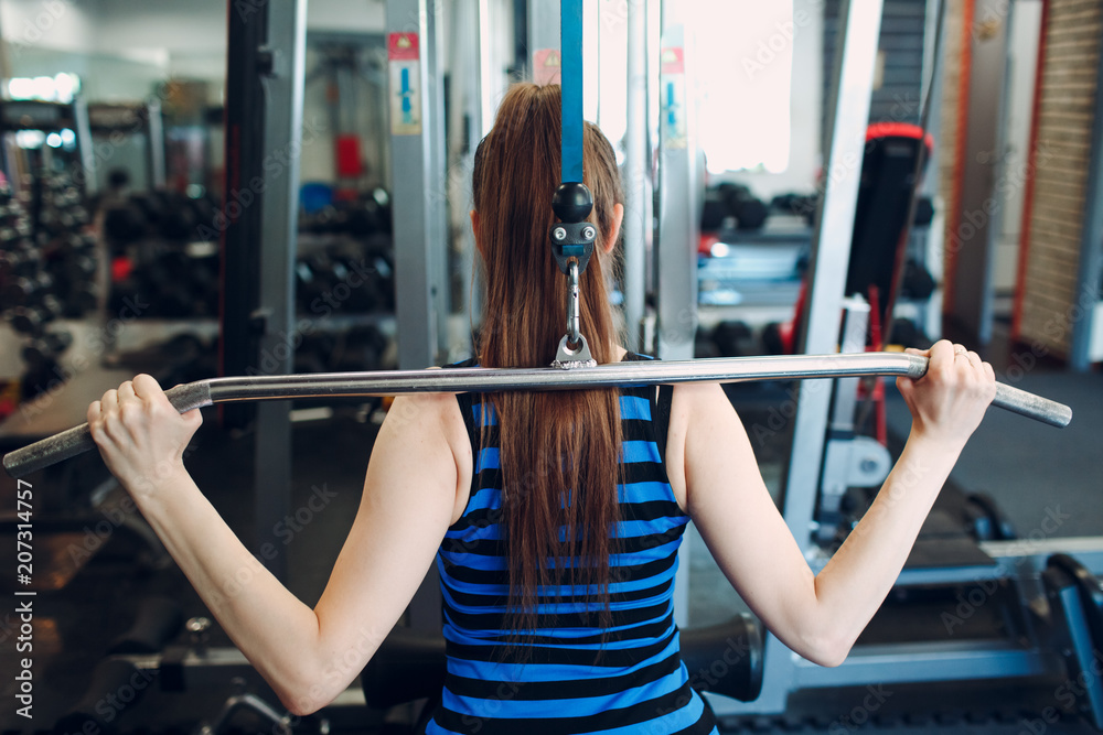 Athletic woman using machine for pumping back muscles Athletic woman using machine for pumping back muscles