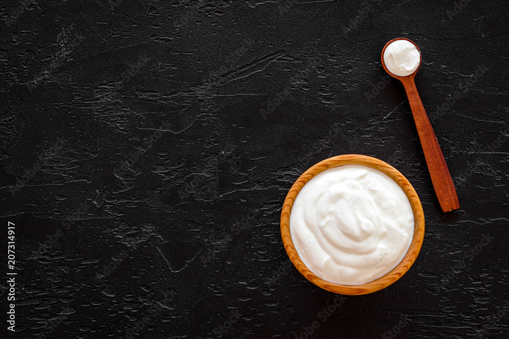 Healthy product, healthy meal. Greek yogurt in brown bowl near spoon on black background top view copy space Healthy product, healthy meal. Greek yogurt in brown bowl near spoon on black background top view copy space