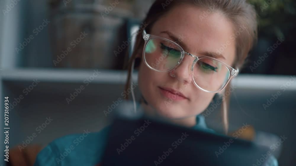 Portrait of pretty, unusual girl. She sits alone in room with headphones, listens to music and uses gadget. Modern girl with a tablet reads a book or communicates on Internet. Portrait of pretty, unusual girl. She sits alone in room with headphones, listens to music and uses gadget. Modern girl with a tablet reads a book or communicates on Internet.