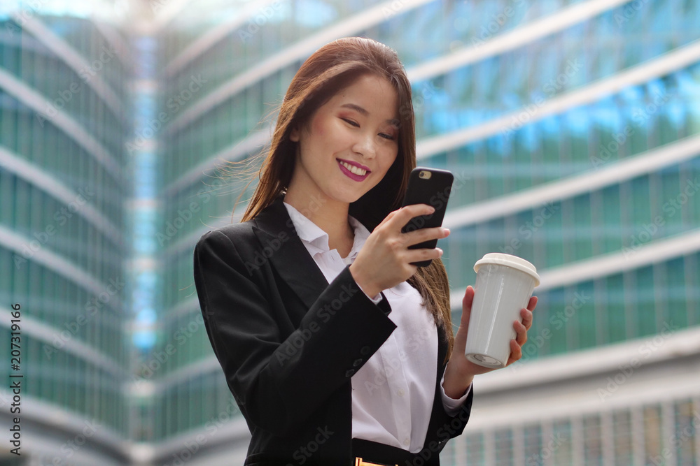 A business woman, she is happy and smiling while sending messages, working emails or calling using the phone, outside the office. Concept of: technology, network, oriental
