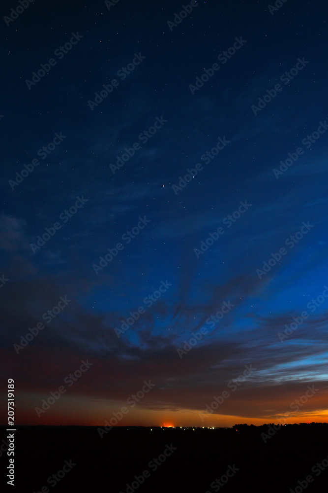 Night sky with stars. A bright sunset with clouds. Cosmic space above the earth's surface. Long exposure.