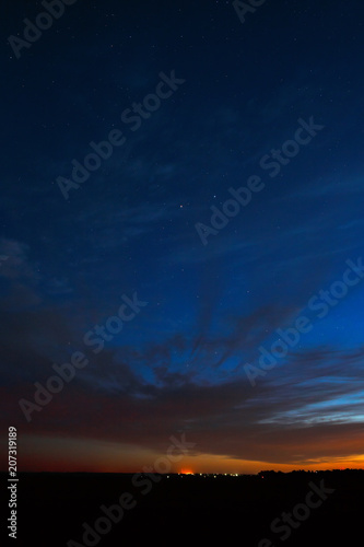 Night sky with stars. A bright sunset with clouds. Cosmic space above the earth's surface. Long exposure.