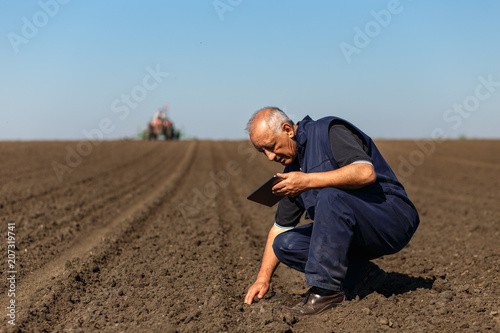 Senior farmer in field examining sowing and holding tablet in his hands.