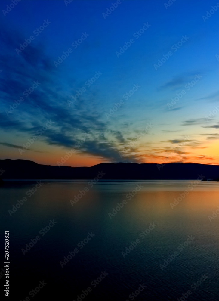 Orange sunrise reflect in dark calm water surface of lake Baikal early morning. Summer landscape sunrise over water with silhouette mountain range on another shore lake
