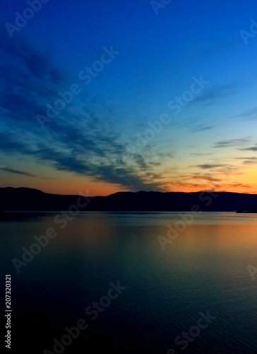 Orange sunrise reflect in dark calm water surface of lake Baikal early morning. Summer landscape sunrise over water with silhouette mountain range on another shore lake © Вера Тихонова
