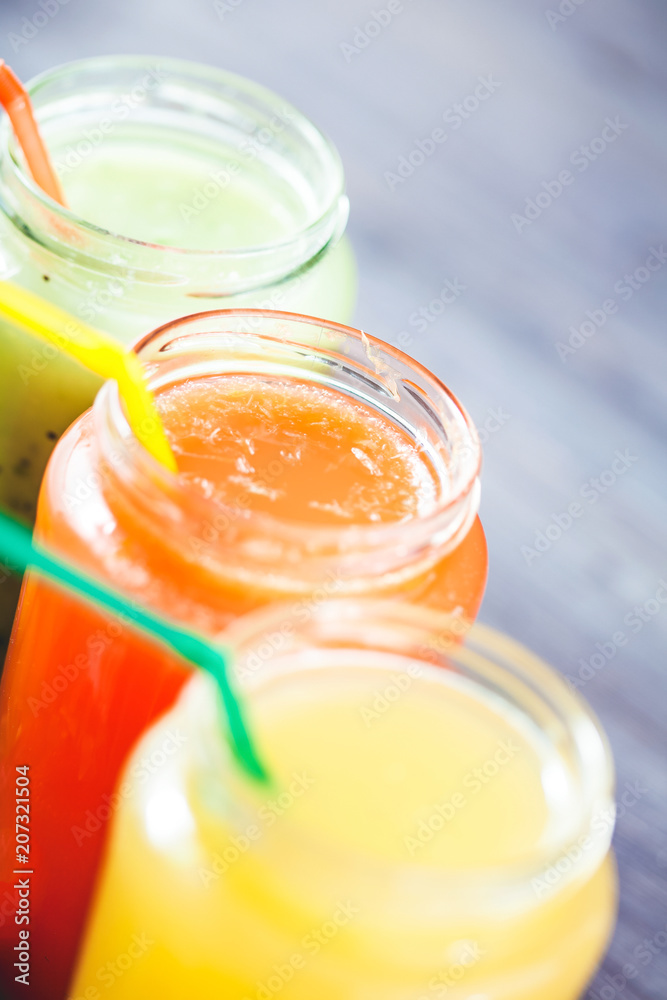 freshly squeezed fruit juice, smoothies yellow orange green blue banana lemon apple orange kiwi grape strawberry on a dark wooden background Close up freshly squeezed fruit juice, smoothies yellow orange green blue banana lemon apple orange kiwi grape strawberry on a dark wooden background Close up