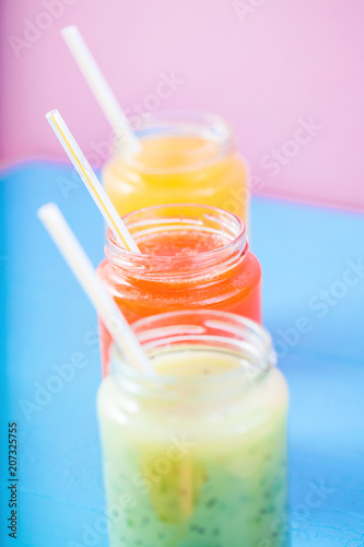 freshly squeezed fruit juice, smoothies yellow orange green on bright blue and pink background Close - up