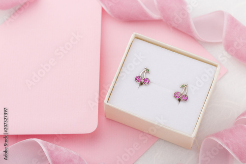 Cherry shaped earrings with crystals in gift box on pink envelope background with copy space