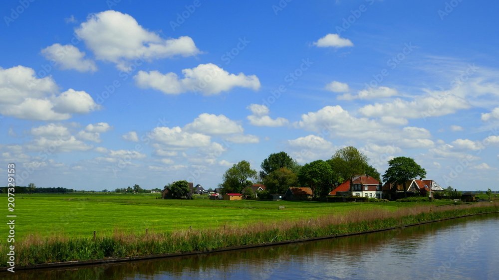 flache Landschaft in Friesland mit Kanal, grünen Wiesen, Bauernhöfen und herrlichen Wolken