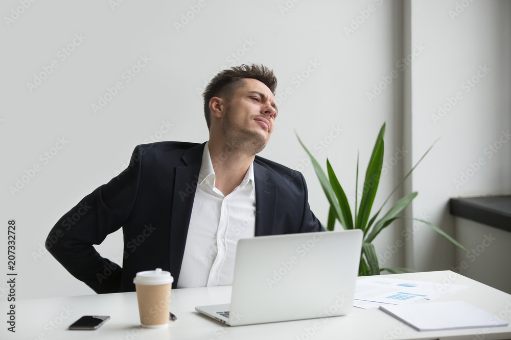 Upset businessman touching aching back feeling strong backache pain in tensed muscles sitting on uncomfortable office chair at work, incorrect posture and sedentary computer work problems concept Upset businessman touching aching back feeling strong backache pain in tensed muscles sitting on uncomfortable office chair at work, incorrect posture and sedentary computer work problems concept