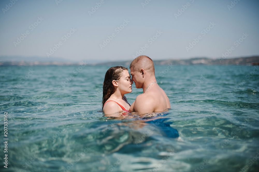 Close up of sensual young couple of man and woman hugging and kissing in turquoise sea water on vacation in Greece Close up of sensual young couple of man and woman hugging and kissing in turquoise sea water on vacation in Greece