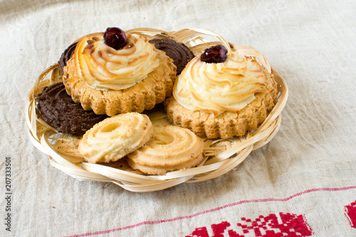 Traditional Russian pastry vatrushka or sochnja, homemade open patties with cottage cheese, round buns, cheesecake, curd patty in wooden plate on homemade tablecloth background, close-up photo