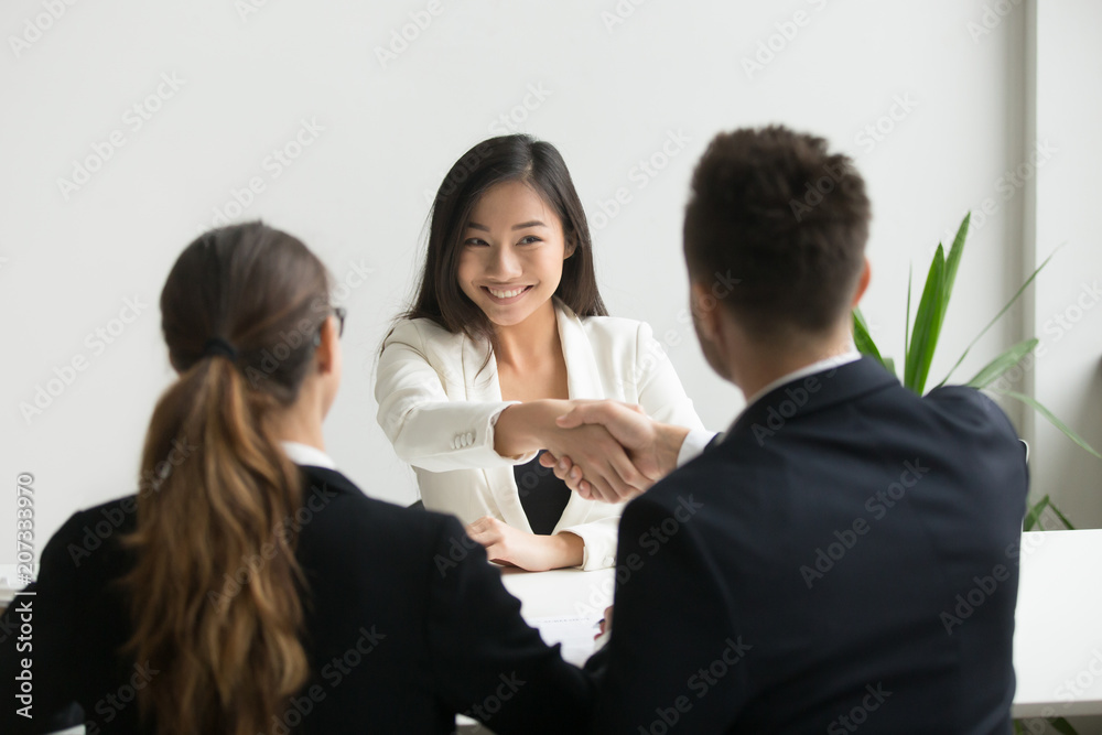 Happy millennial asian applicant getting hired shaking hand of hr, employer handshaking successful smiling chinese candidate congratulating with job interview win offering employment contract concept Happy millennial asian applicant getting hired shaking hand of hr, employer handshaking successful smiling chinese candidate congratulating with job interview win offering employment contract concept