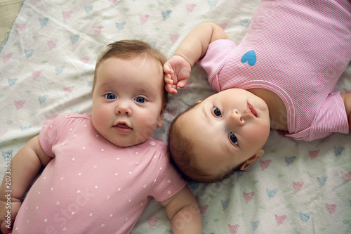 two sisters twins baby in pink clothes lying on the bed photo
