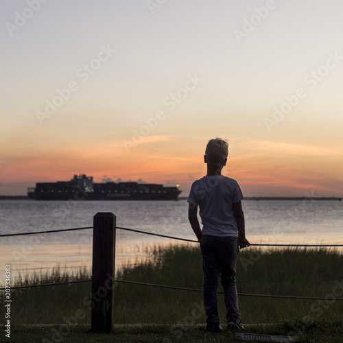 Boy watching a ship pull into Charleston Harbor at sunset