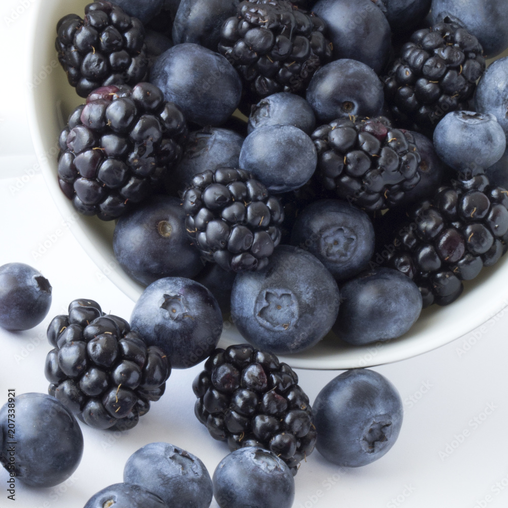 Blueberries and blackberries overflowing and spilling out of container Blueberries and blackberries overflowing and spilling out of container