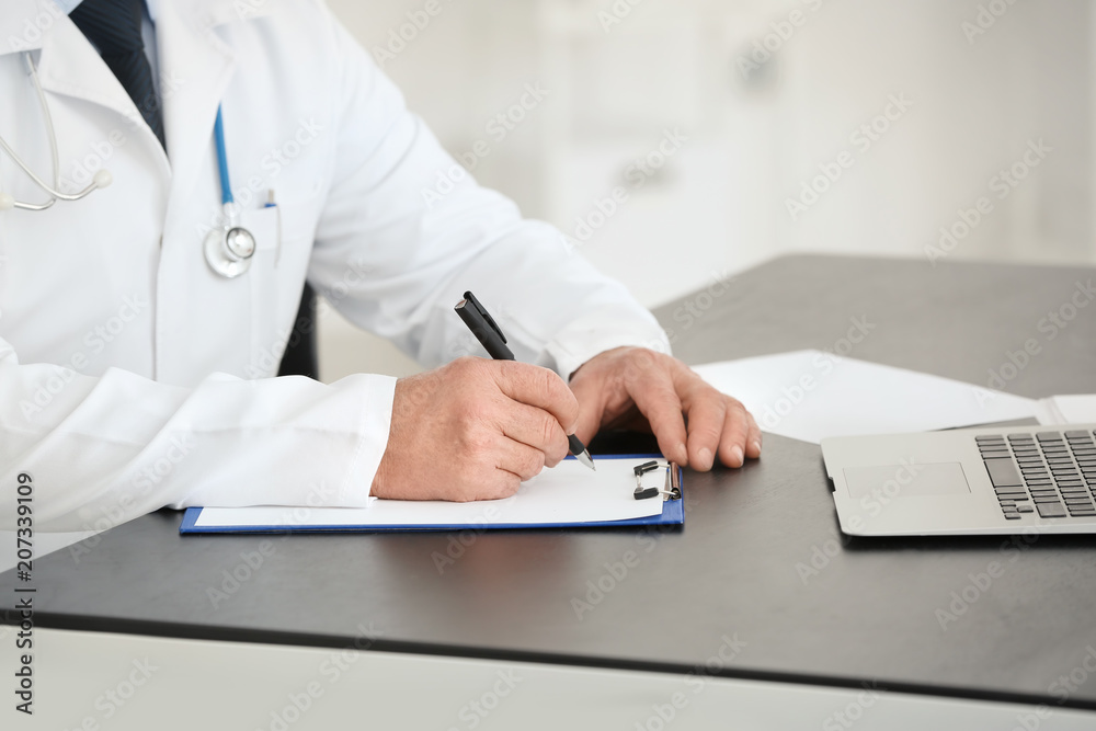 Fototapeta premium Male doctor filling up application form in consultation room, closeup