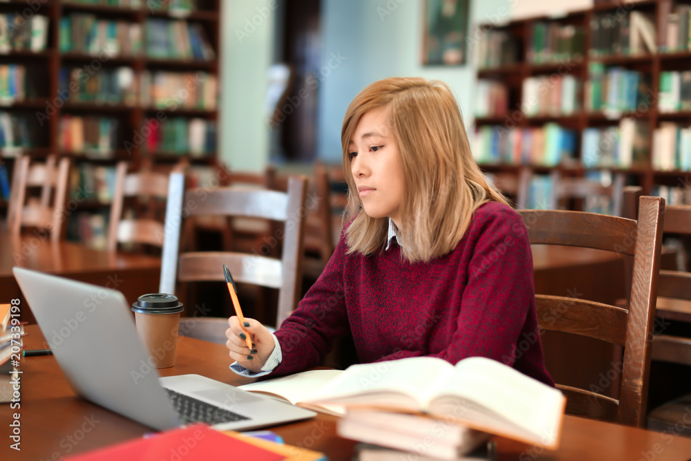 Asian student with laptop studying in library Asian student with laptop studying in library