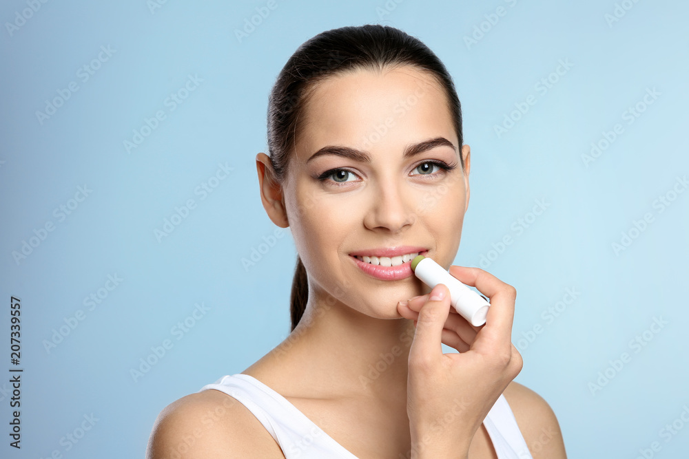 Young woman applying balm on her lips against color background Young woman applying balm on her lips against color background