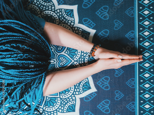 Concentrated woman with blue african braids praying with wooden rosary mala beads. Namaste. Close up hands on yoga mat with mandala. Top view.