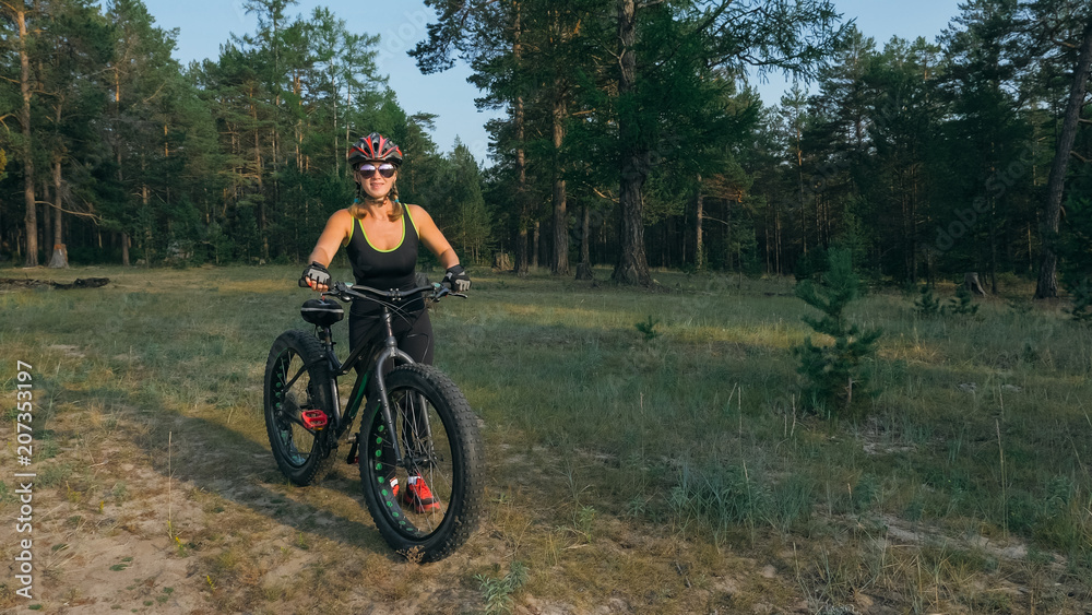 Fototapeta premium Fat bike also called fatbike or fat-tire bike in summer riding in the forest. Beautiful girl and her bicycle in the forest. She rolls her bike and poses to the operator.