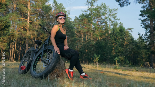 Fototapeta Naklejka Na Ścianę i Meble -  Fat bike also called fatbike or fat-tire bike in summer riding in the forest. Beautiful girl and her bicycle in the forest. She poses and smiles to the operator. Very positive and provocative.