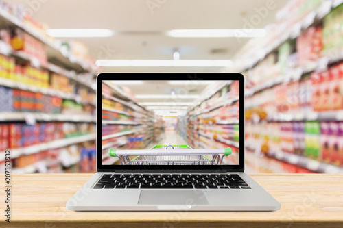 laptop computer on wood table with supermarket aisle blurred background online shopping concept photo