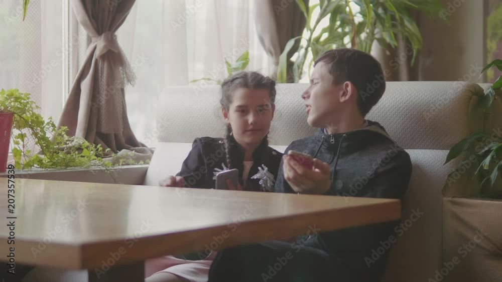 Stylish family sitting in a city cafe look in the phone and take selfies and smile on the sunny city background. Little girl show finger to the top looking at camera. True emotions, good mood.