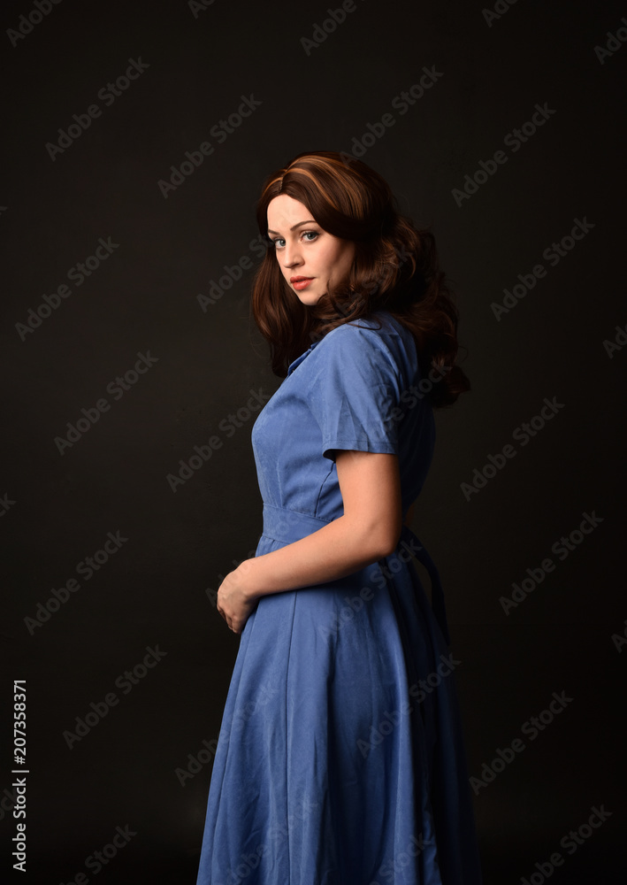 3/4 portrait of brunette lady wearing blue dress, facing away from camera. posed on black studio background. 3/4 portrait of brunette lady wearing blue dress, facing away from camera. posed on black studio background.