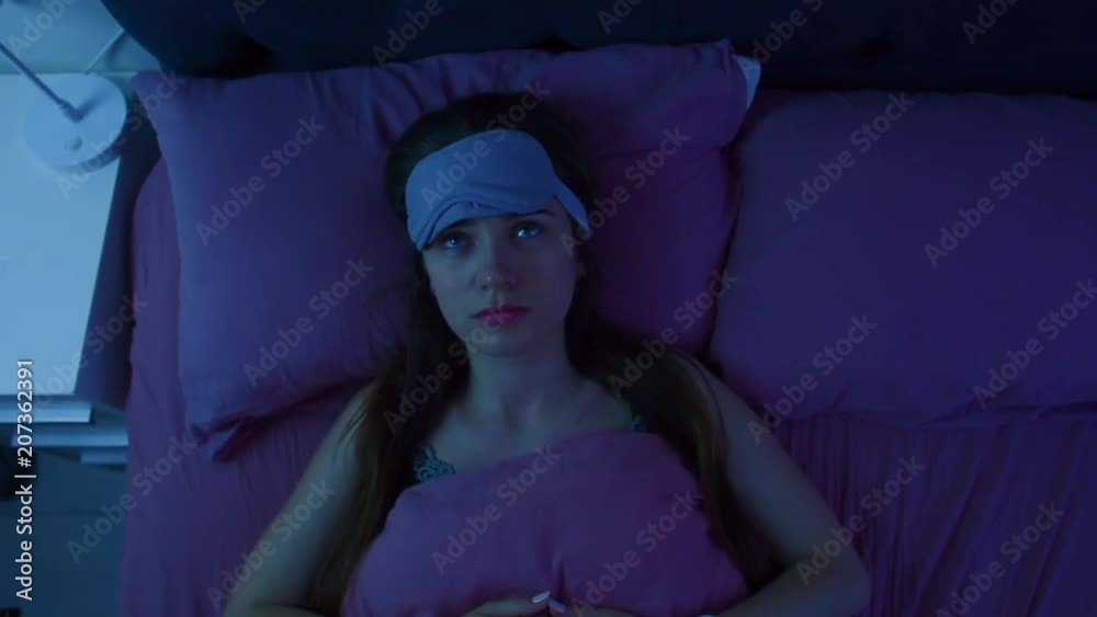 Young attractive awake girl can't sleep because of insomnia. Apatic woman disturbed by the noise made by neighbours is staring at the ceiling. Top view.