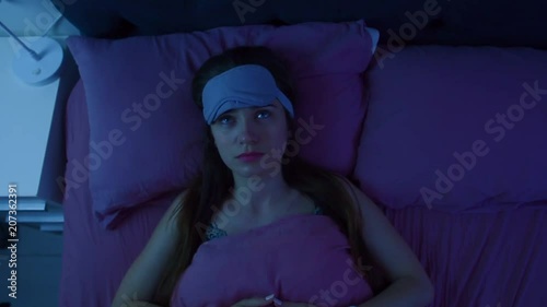 Young attractive awake girl can't sleep because of insomnia. Apatic woman disturbed by the noise made by neighbours is staring at the ceiling. Top view.