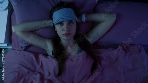 Young attractive awake girl can't sleep because of insomnia. Apatic woman disturbed by the noise made by neighbours is staring at the ceiling. Top view.