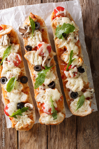 Italian sandwiches pizza casserole: cut baguette baked with chicken, cheese, tomatoes, olives and mushrooms close-up. Vertical top view