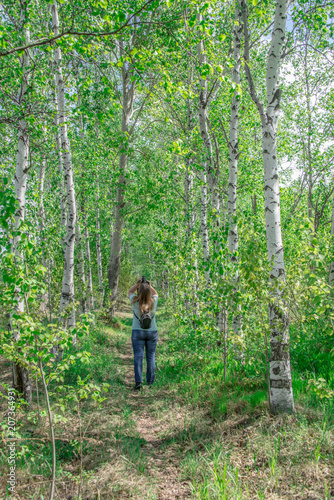 Girl with a backpack on his back travels, stands back in a birch grove in the spring