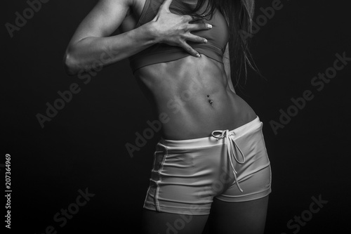 Beautiful athletic woman shakes her abdominal muscles on dark background