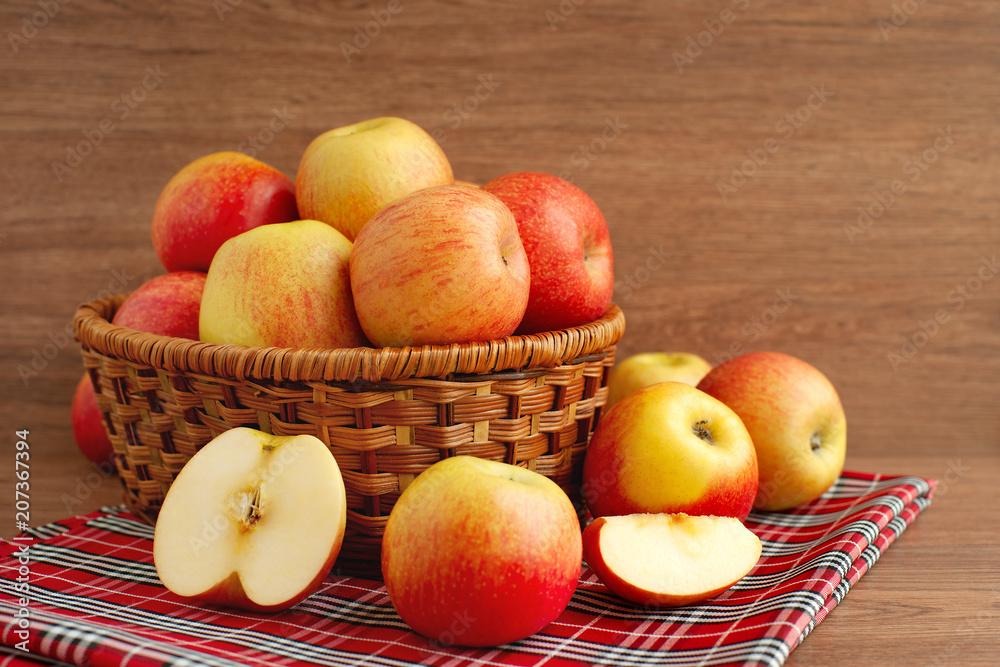 Harvest of apples in a wicker basket. Many colorful apples in a large wicker basket on a wooden background. Fruits are collected in the garden. Harvest of apples in a wicker basket. Many colorful apples in a large wicker basket on a wooden background. Fruits are collected in the garden.
