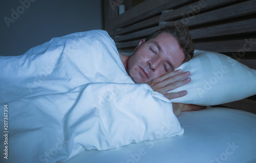 young attractive and handsome tired man on his 30s or 40s in bed sleeping covered with duvet peacefully and relaxed at apartment bedroom resting