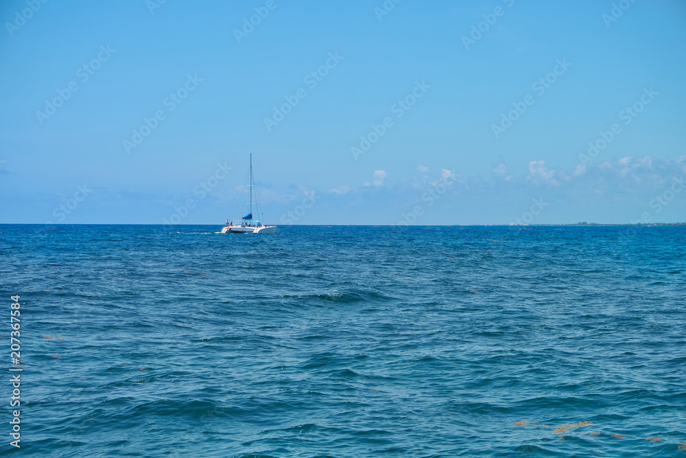 Obraz premium Sailing yacht catamaran sails on the waves in the warm Caribbean Sea. Sailboat. Sailing. Cancun Mexico. Summer sunny day, blue sky with clouds.