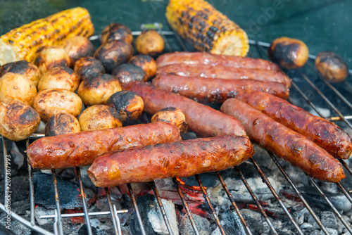 Baked potatoes, corn and sausages on a barbecue grill