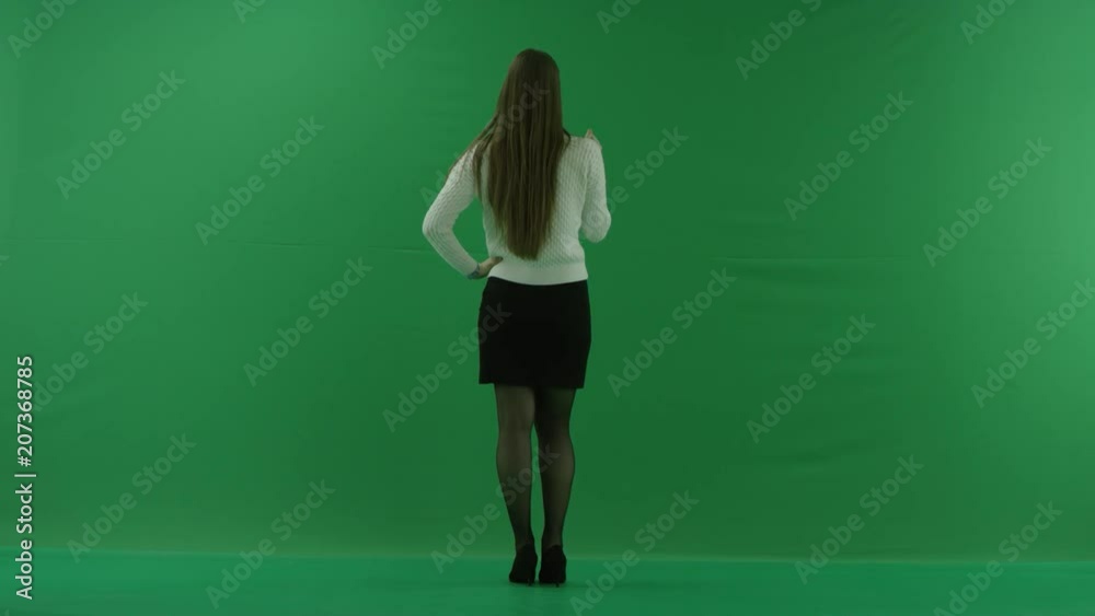 young woman stands back to the camera, scrolls the screen and considers something on green screen young woman stands back to the camera, scrolls the screen and considers something on green screen