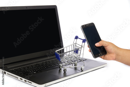 Shopping cart over a laptop computer with hand holding mobile on white background. shopping online concept.
