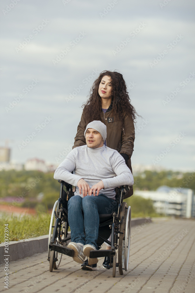 Disabled man in a wheelchair with young woman walking at the city street  Stock Photo | Adobe Stock