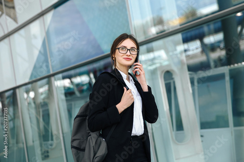 Airport woman on smart phone at gate waiting in terminal. Air travel concept with young casual business woman sitting with talking on the smartphone, carry-on hand luggage trolley. Beautiful young.