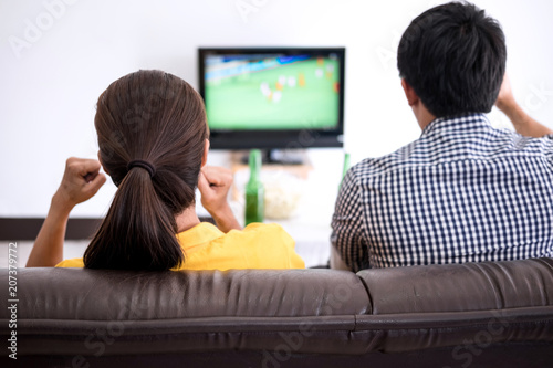Young Asian couple love watching soccer match on tv and cheering football team, celebrating with beer and popcorn at home, sports and entertainment concept